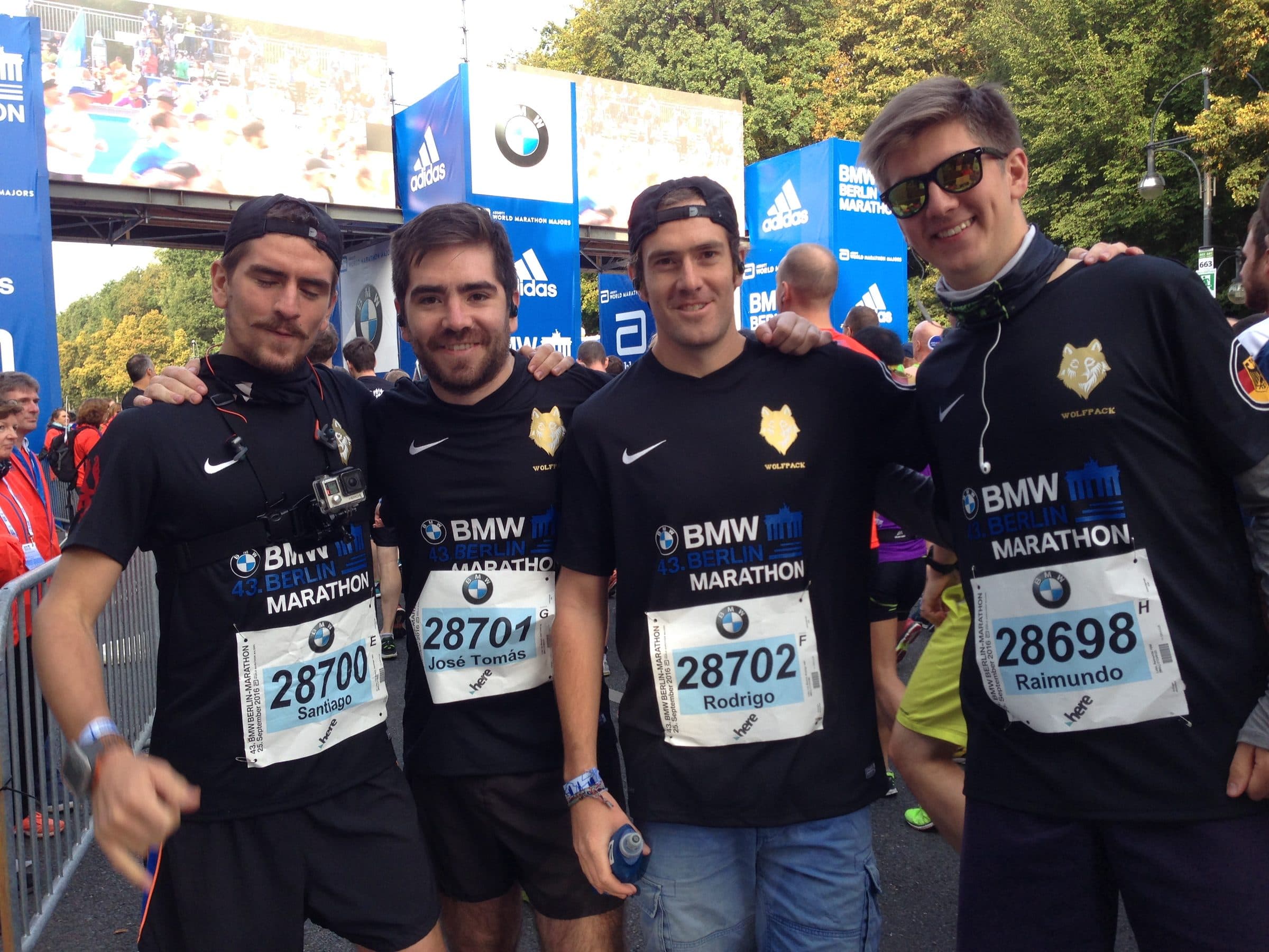 The six runners laughing together in the start area, race numbers pinned on.