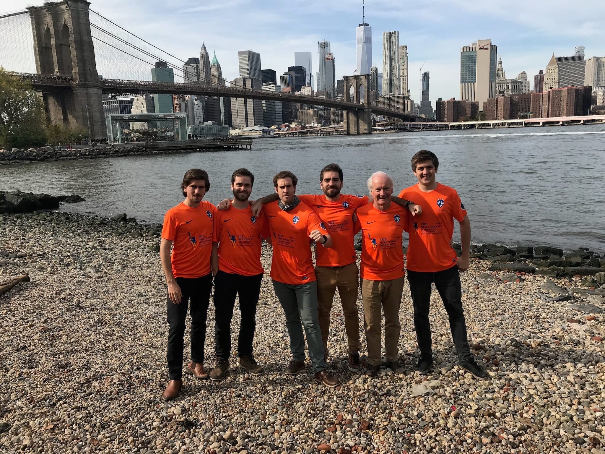 Los seis corredores con camisetas naranjas de Nueva York, con el Puente de Brooklyn y el horizonte detrás.
