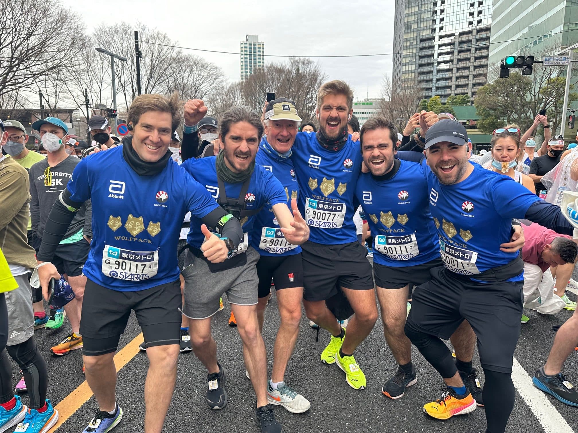 El padre y sus cinco hijos con camisetas azules del Maratón de Tokio, abrazados y con los puños en alto, en la línea de partida en 2023.